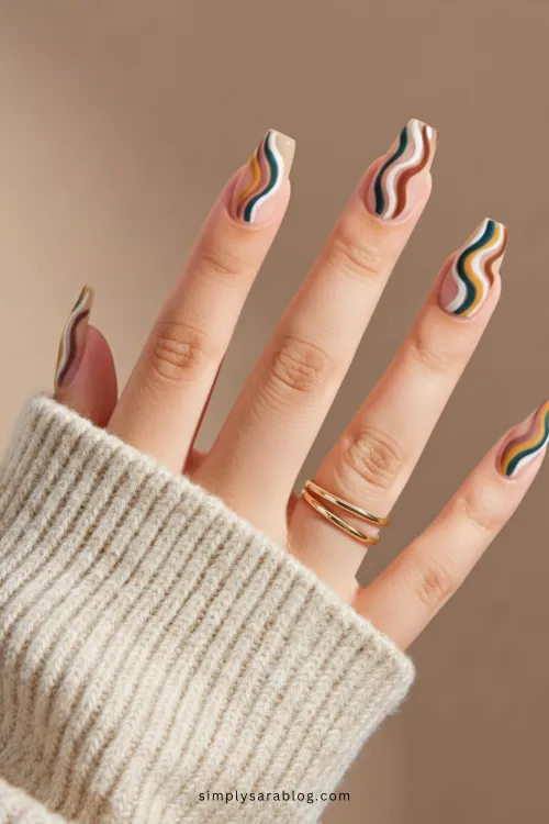 Almond-shaped nails with blush pink polish, accented with gold foil and tiny white flowers, held against a white sweater backdrop